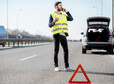 Man in vest calling road assistance standing near the broken car on the highway