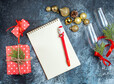 Top view of glass goblets with red ribbon and decoration accessories next to gift boxes notebook with pen on dark background